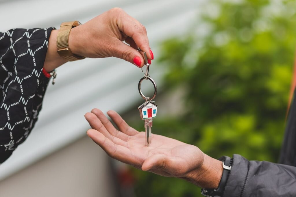 Close-up of a hand handing over a key with a house keychain, symbolizing real estate transaction.